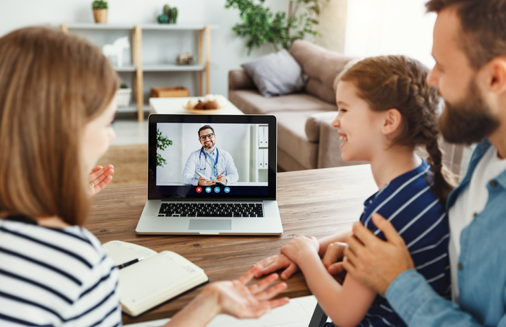 Imagen de padres e hija sentados en la mesa y hablando con un médico por teleconsulta desde su casa